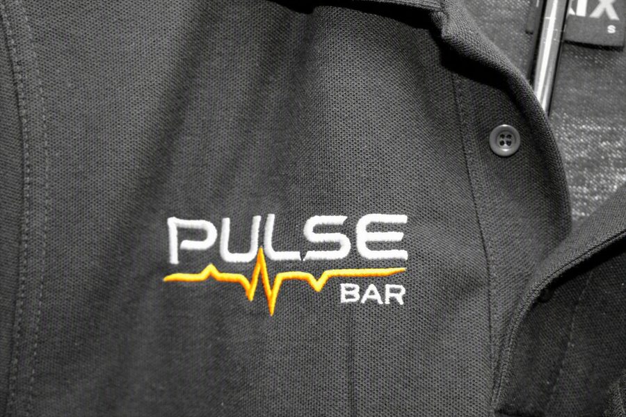 Pulse Bar logo embroidered in white and orange on a black polo shirt by SVP Southend Embroidery