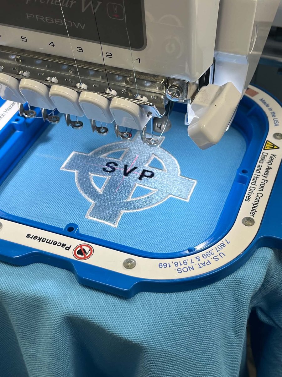SVP cross logo being embroidered on blue fabric in a Brother PR680W embroidery machine hoop at SVP Southend